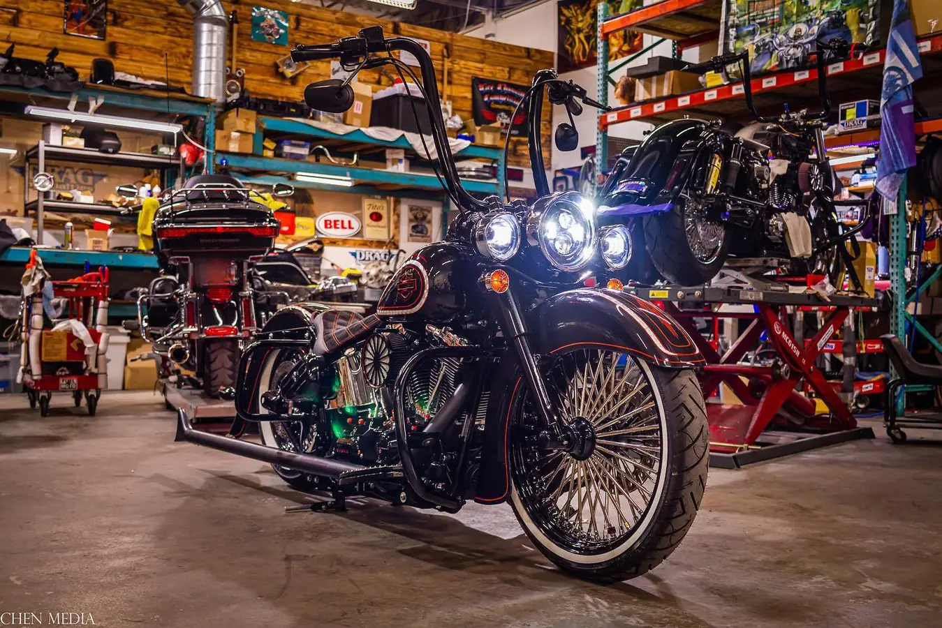 The same pinstriped Softail with whitewall tires and lights on, inside a motorcycle shop