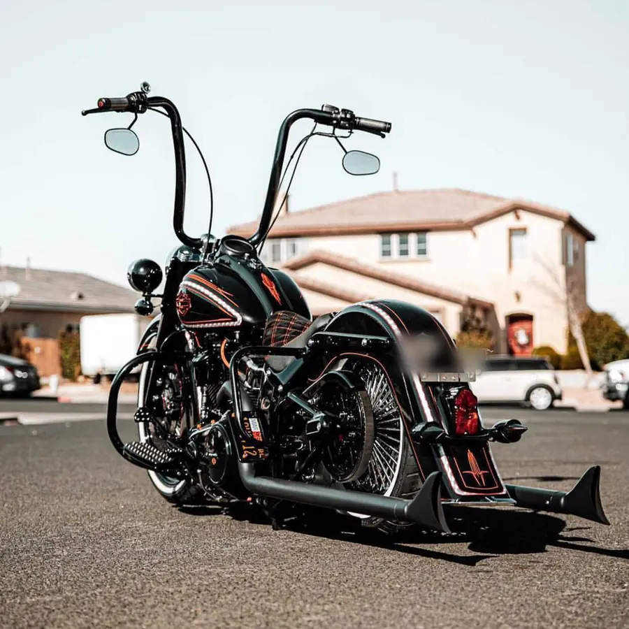 Black Softail with ape-hanger bars, pinstriping, and fishtail pipes parked on a residential street